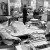 Black and white photo of woman at an office, one reads the newspaper