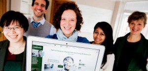 5 people smiling, old holds up Kickstarter page on laptop