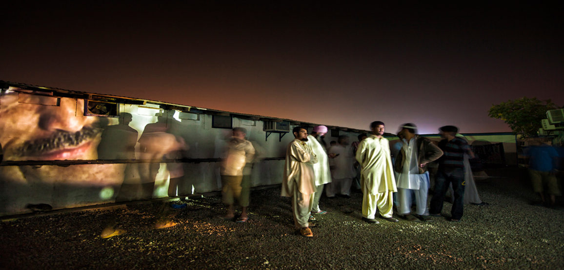 Photos projected on Dubai trailer homes surrounding by onlookers