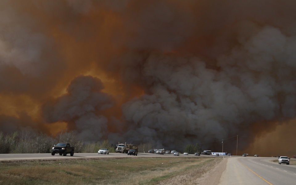 Cars driving on highway away from sky full of smoke and tinted orange