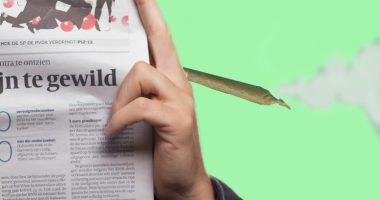 A person reads a newspaper while holding a marijuana cigarette