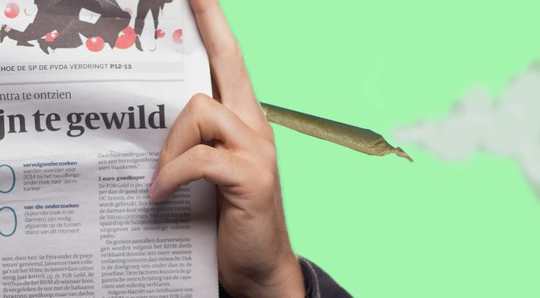 A person reads a newspaper while holding a marijuana cigarette