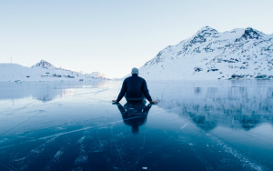 A person sits on an ice-covered lake with their back to the camera
