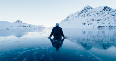 A person sits on an ice-covered lake with their back to the camera