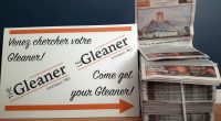 A white sign reading "Come get your Gleaner" in English and French points to a stack of newspapers.