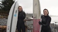 Two women stand with surf boards