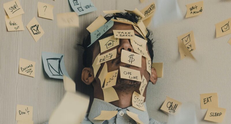 A young man lies on the ground, his face covered in sticky notes
