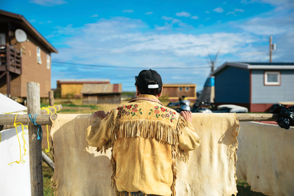 George Cleary, a former Deline chief, wears a jacket made of caribou and looks out over the community while standing against a drying moose hide.
