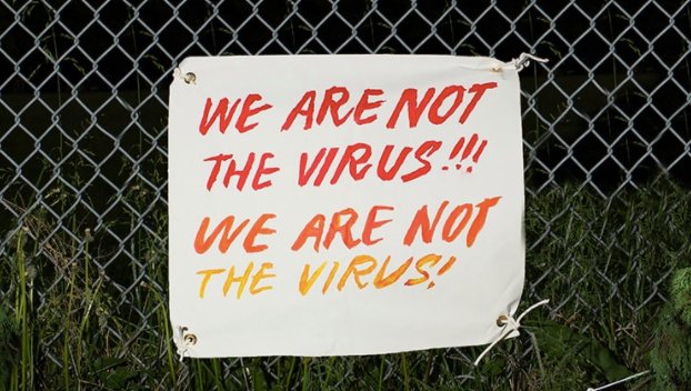 Sign on a fence that says we are not the virus, we are not the virus.